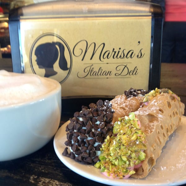 Marisa's Italian Deli sign behind a cappuccino and two cannolis, one with chocolate chips, one with pistachios.
