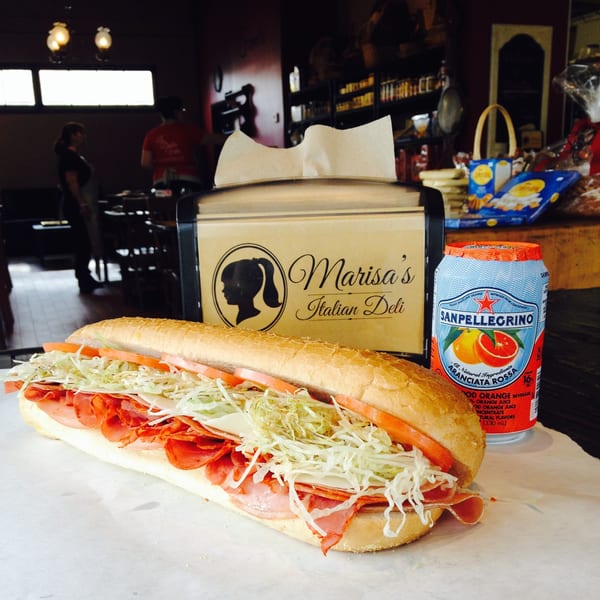 A large Italian deli sub with meats, cheese, lettuce, and tomatoes next to a San Pellegrino can.