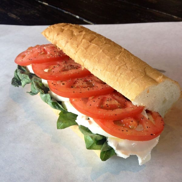 A fresh Italian deli sandwich with sliced tomatoes, mozzarella, and basil on a baguette.