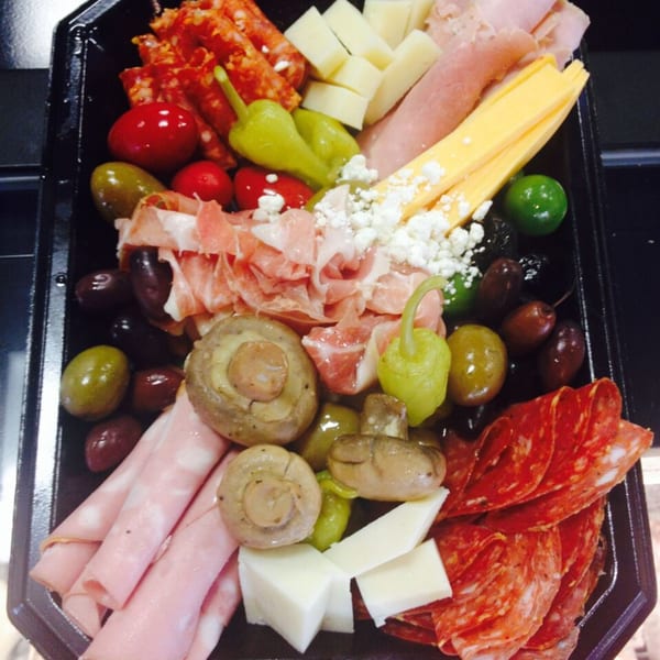 A black platter filled with Italian deli meats, cheeses, olives, mushrooms, and peppers.